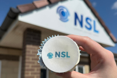 Image of a branded Northern Safety cupcake being held up in front of Northern Safety's building. 